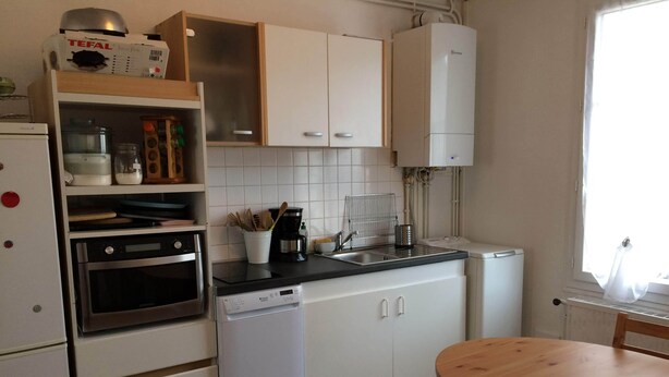 A modern kitchen with white cabinets, a built-in oven, a dishwasher, and a wooden dining table. - Apartment-cottage of the church (Châteauneuf-sur-Loire)