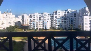 Vista de uma área residencial com edifícios brancos, céu azul claro e uma piscina em primeiro plano.