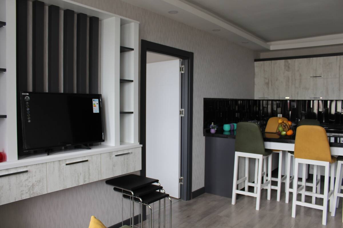 Eine moderne Küche mit Einbauofen, einem Essbereich mit Barhocker und einem an der Wand befestigten Fernseher.