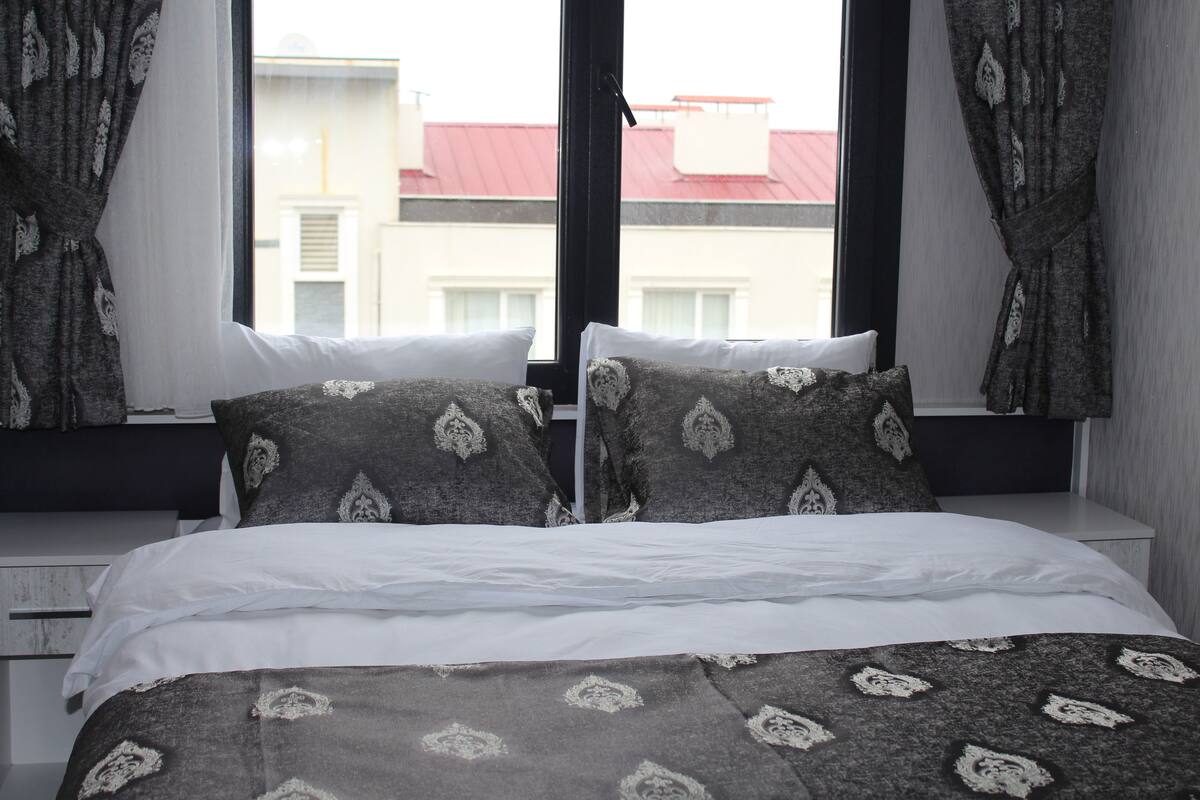 Ein Schlafzimmer mit einem Bett, weißer Bettwäsche, gemusterten Kissen und Vorhängen.