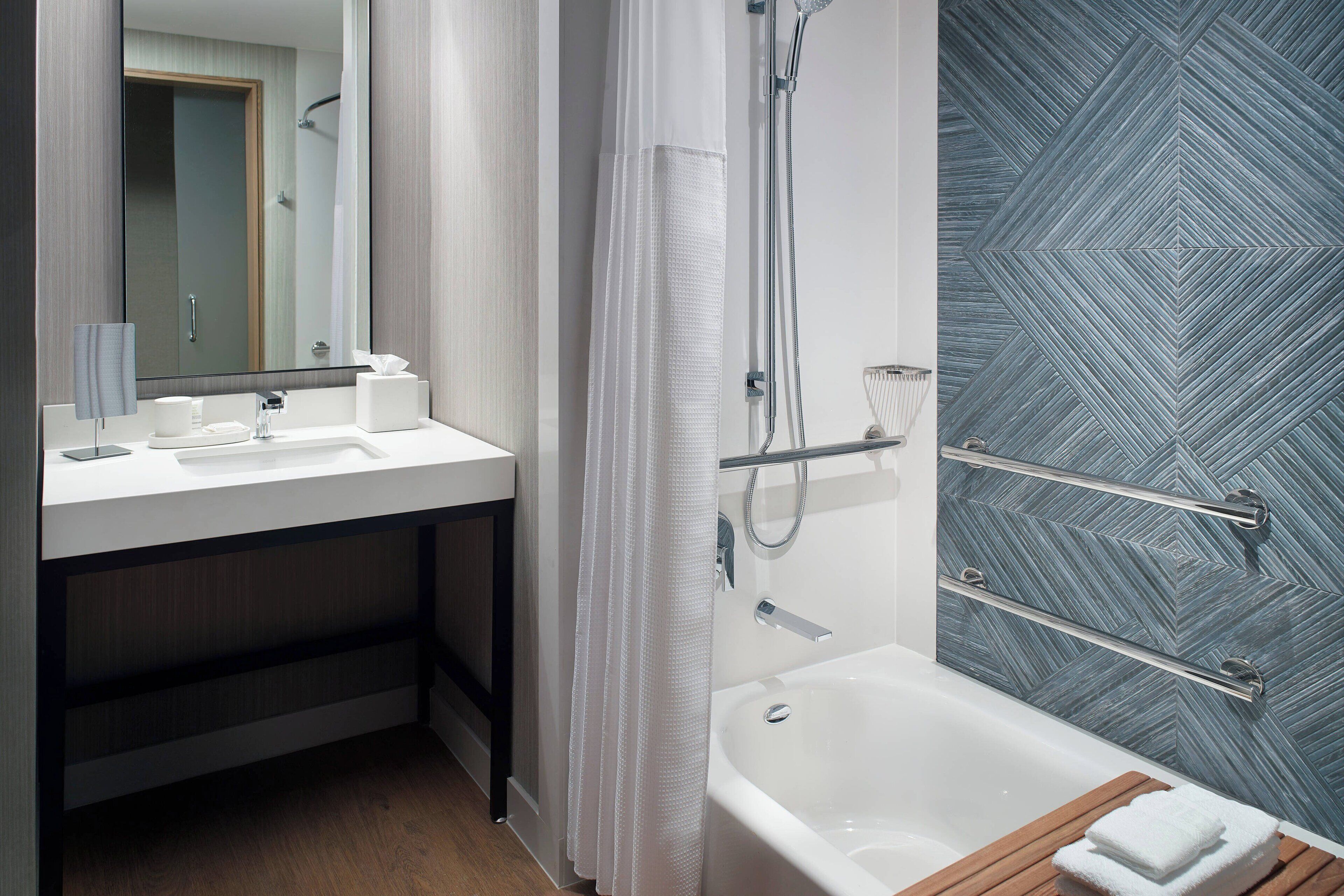 A modern bathroom with a white sink, mirror, and bathtub.