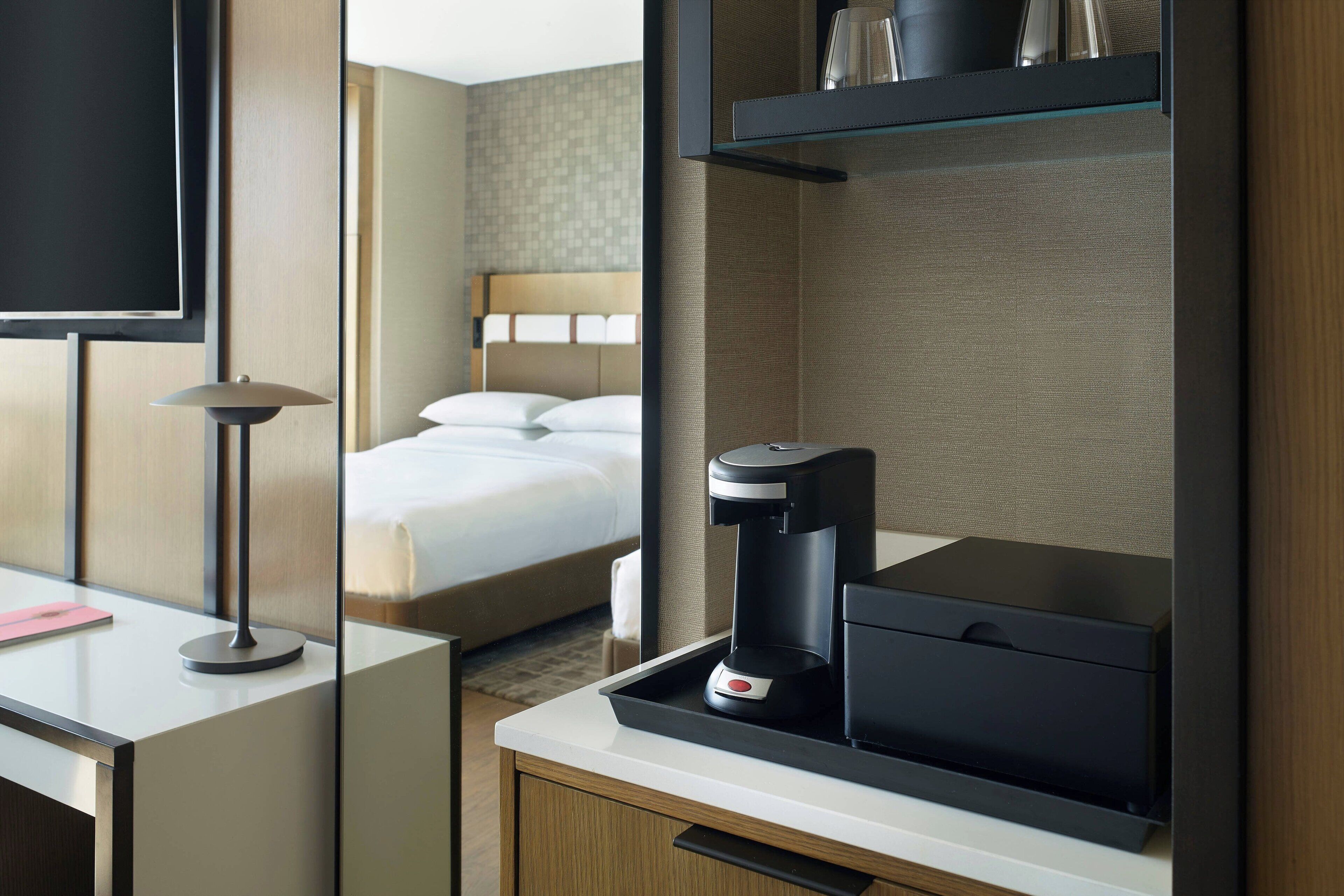 A hotel room with a bed, a desk with a lamp, a coffee maker, and a TV.