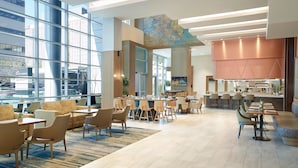 Un moderno vestíbulo de hotel con un amplio espacio de estar, un bar y vistas de la ciudad a través de ventanales del suelo al techo.