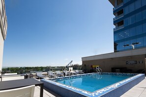 En pool på taket med solstolar och utsikt över stadens silhuett.