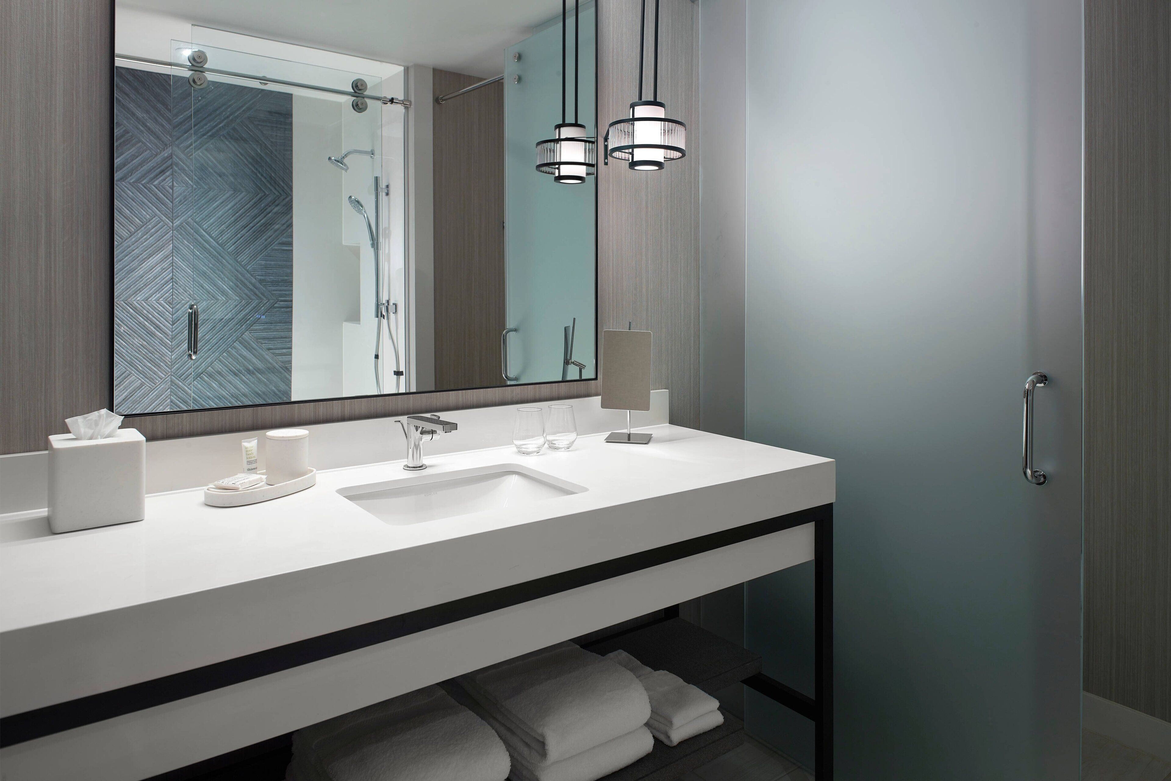 A modern bathroom with a white vanity, a large mirror, and two pendant lights.
