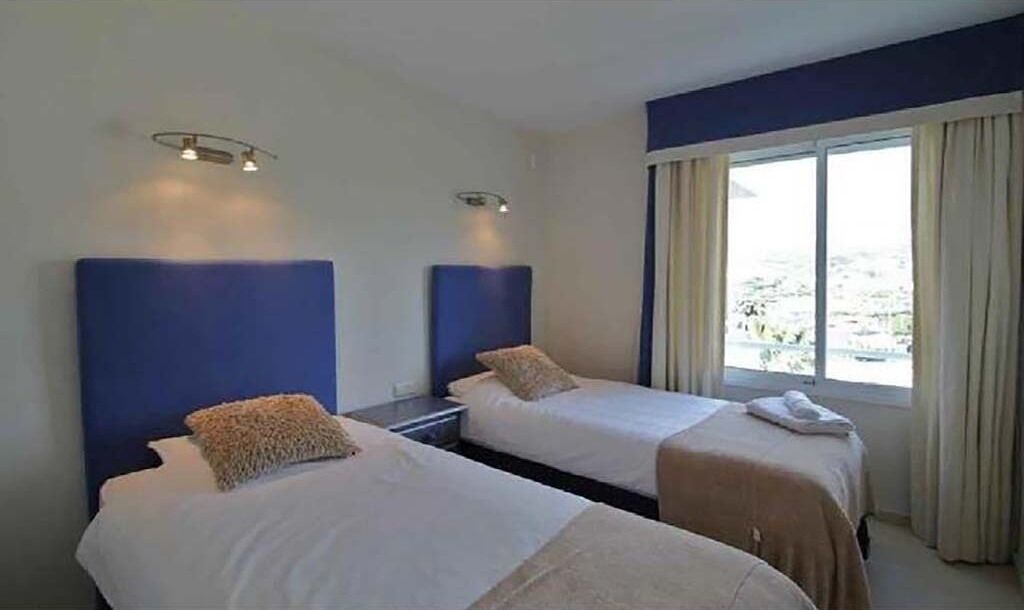 A hotel room with two beds, a large window with curtains, and a view of the city.