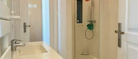 A bathroom with a white sink, a glass shower enclosure, and a door with a handle.