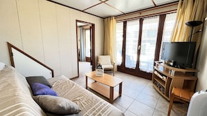 A living room with a sofa, a coffee table, a TV, and a sliding door leading to another room. - VILLA  in the résidence TAMARIS, 4 bedrooms, Wifi, Airco in living room, in PORTIRAGNES PLAGE (PORTIRAGNES)