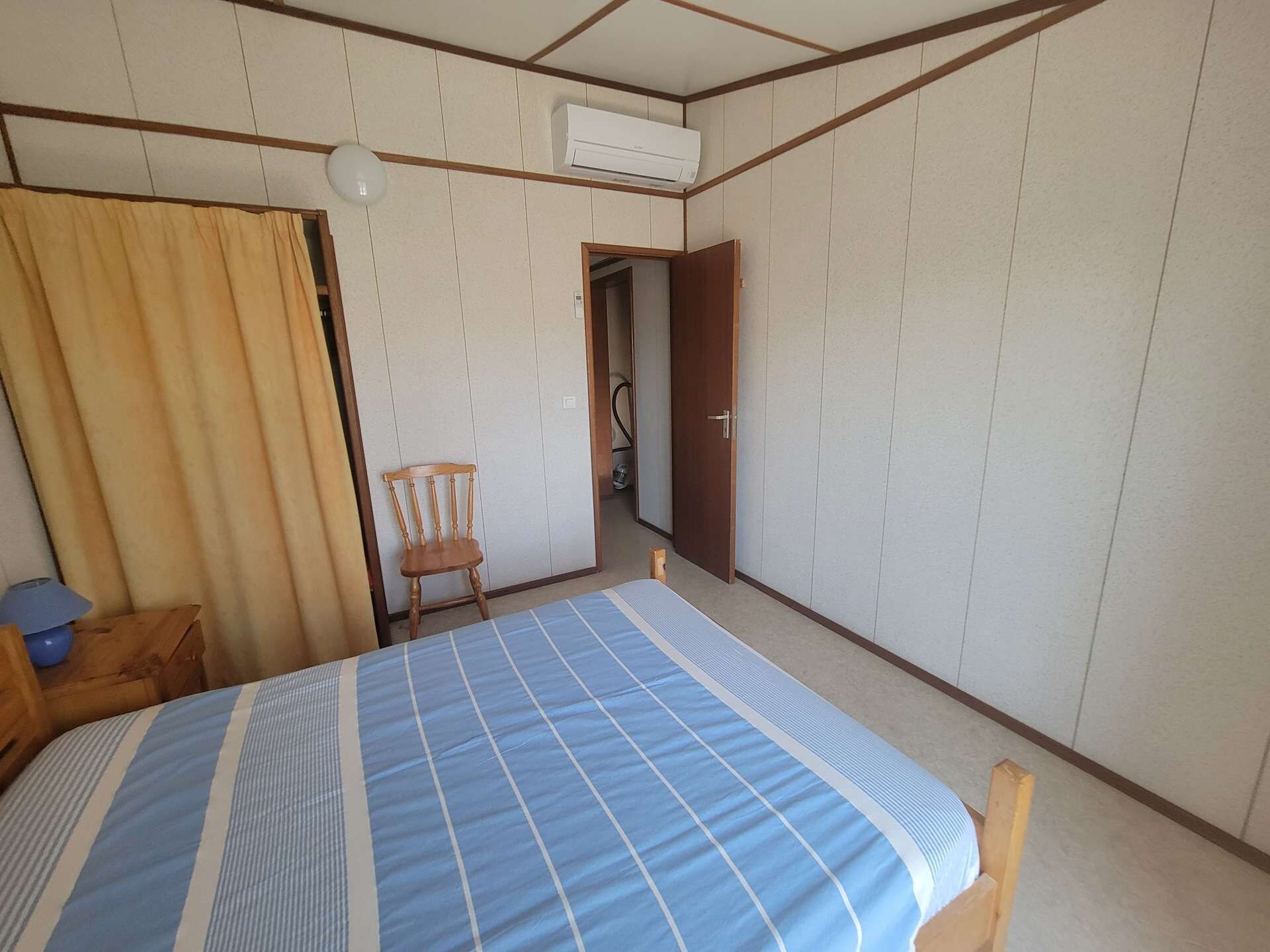 A room with a bed, a chair, an air conditioning unit, and a door leading to another room.