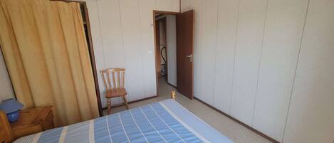 A room with a bed, a chair, an air conditioning unit, and a door leading to another room.