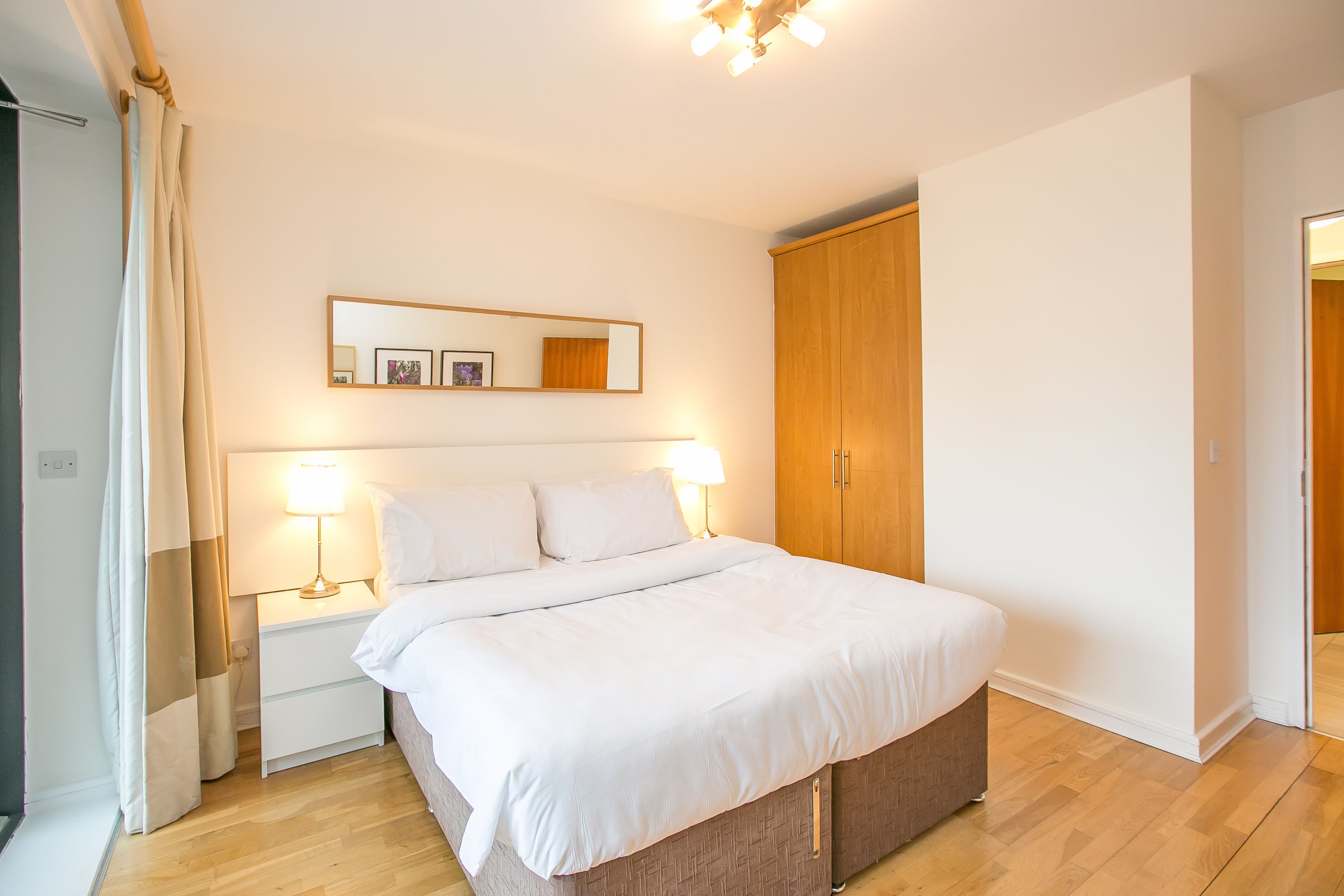 A bedroom with a bed, nightstands, a mirror, and a wardrobe.
