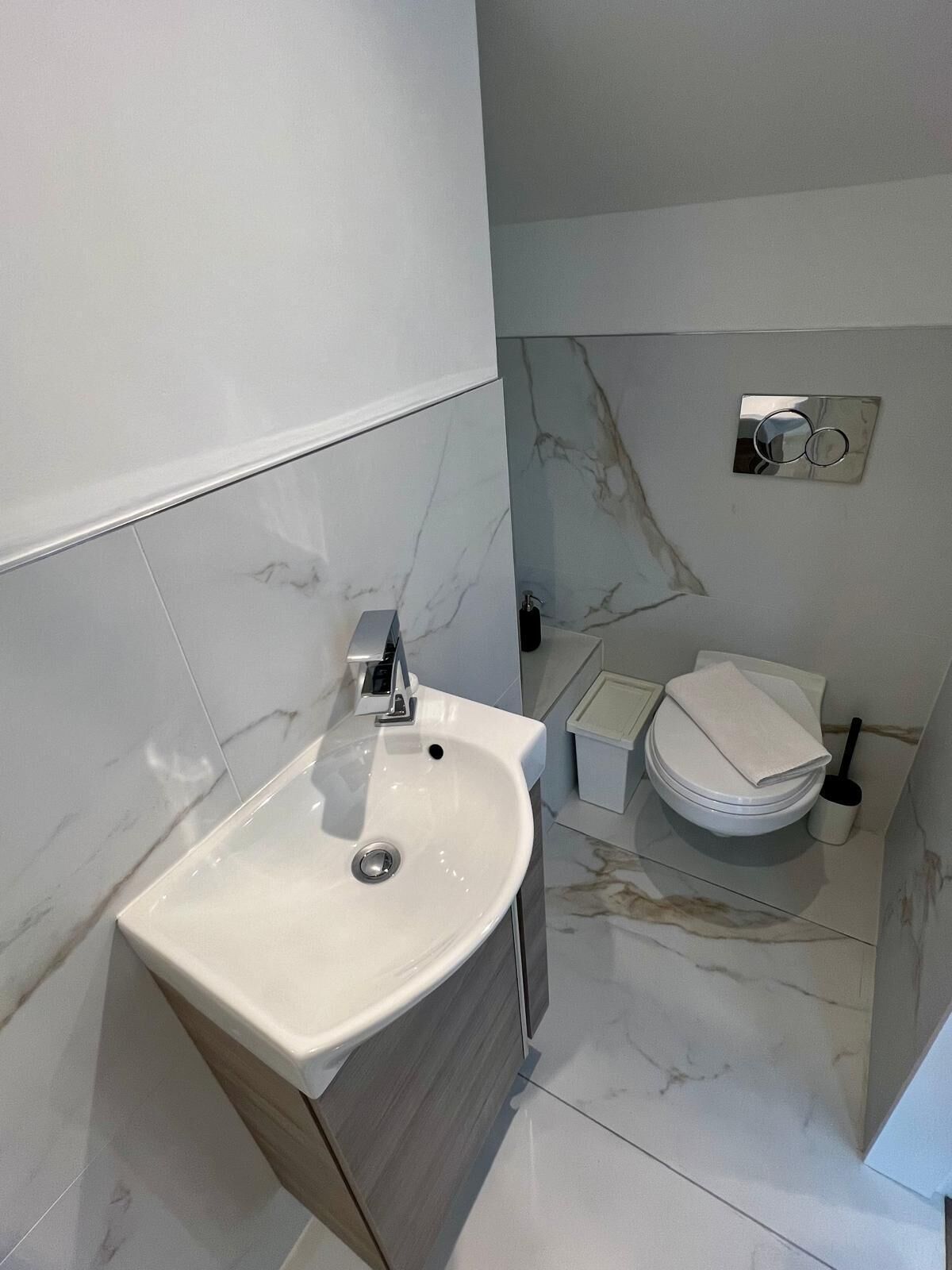 A modern bathroom with a white sink, marble tiles, and a toilet.