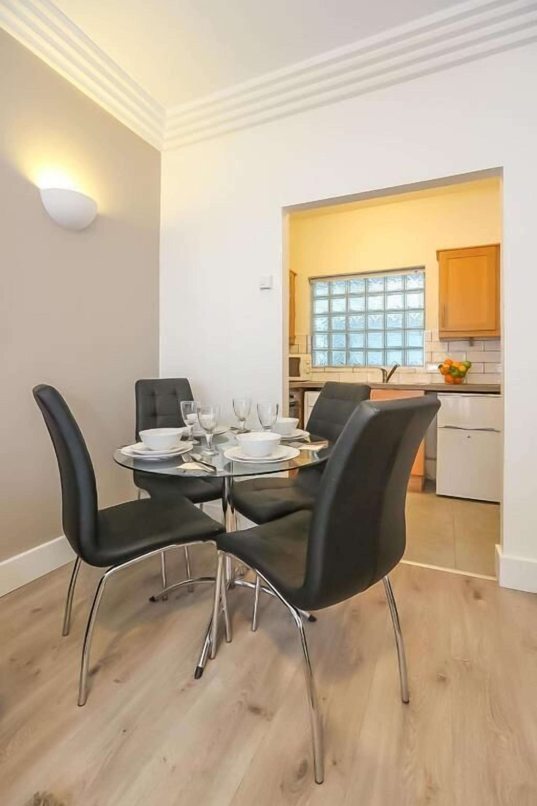 A dining area with a round glass table, black chairs, and a white wall-mounted light.