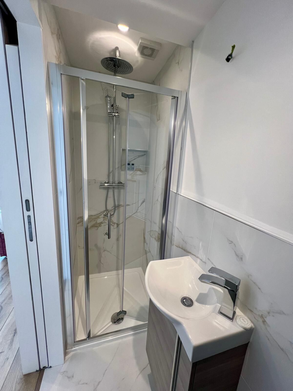 Een moderne badkamer met een douchecabine van glas, een witte wastafel en een marmeren vloer.