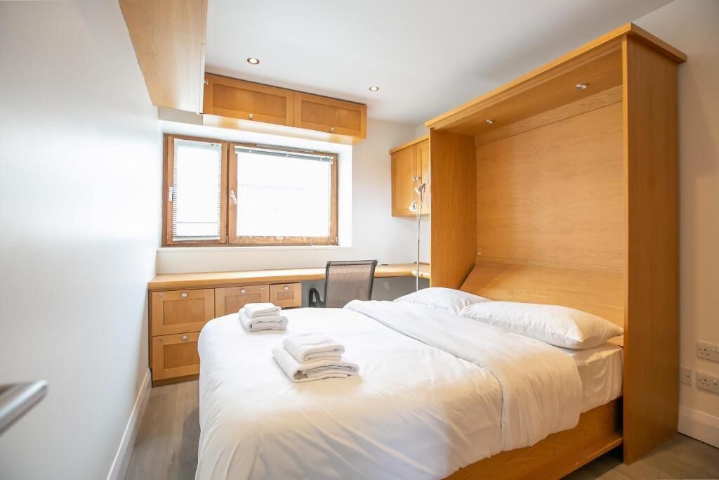 Ein Schlafzimmer mit einem Bett, einem Fenster, Holzsärchen und einem Schreibtisch.
