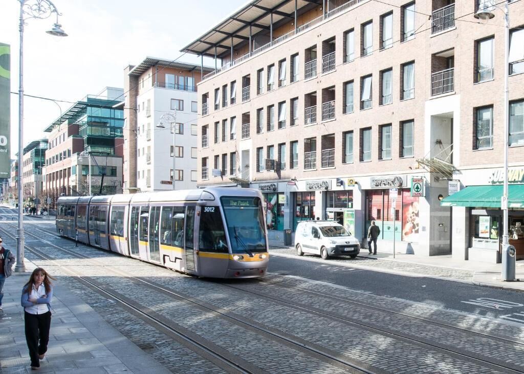 A tram on tracks in an urban setting with buildings and shops.