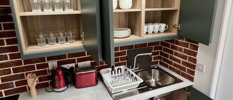 A compact kitchen with wooden shelves, a built-in washing machine, and a sink.