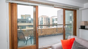 A modern apartment with a balcony, a sofa with cushions, and a view of neighboring buildings. - IFSC Townhouse Apartments (Dublin)