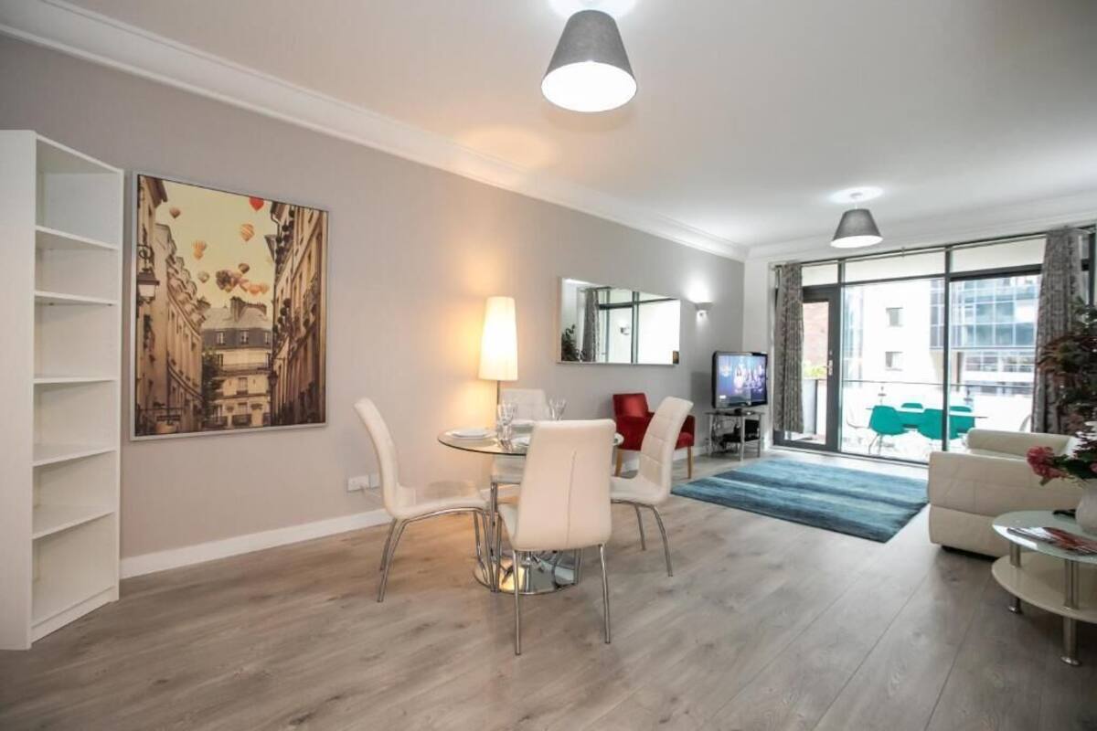 Un salon moderne comprenant un coin repas, un téléviseur et une grande fenêtre donnant sur des immeubles.