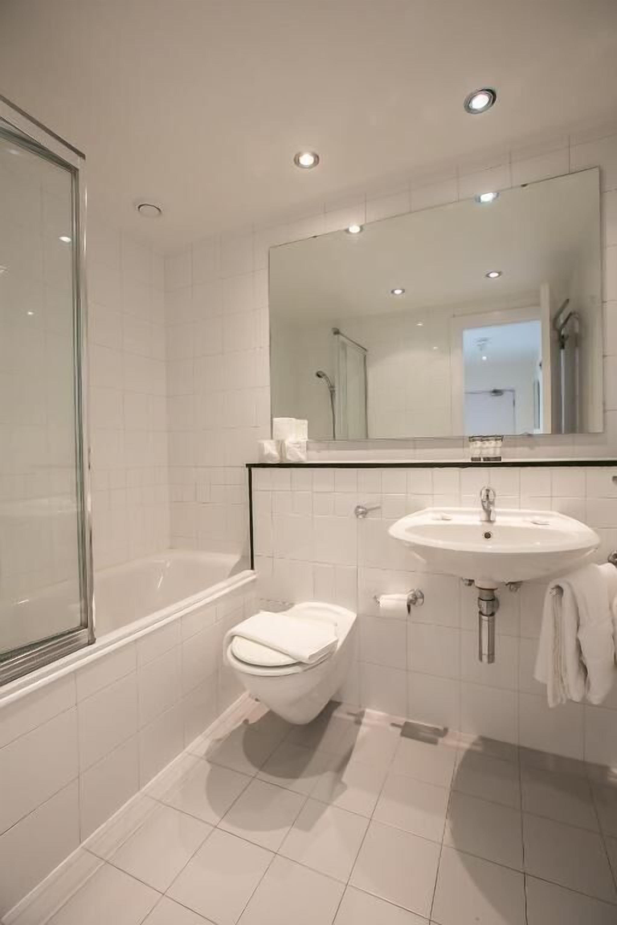 A modern bathroom with a glass shower enclosure, a white toilet, a sink with a mirror above, and a towel hanging on the wall.