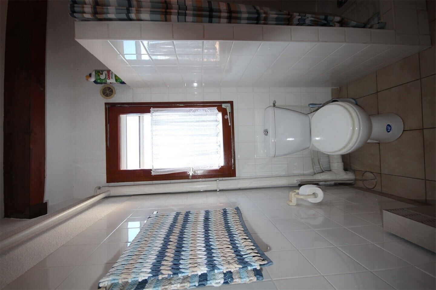 A bathroom with a toilet, a window, and a patterned rug on the floor.