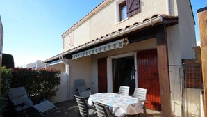 Un patio con tavolo e sedie, una porta rossa e un piccolo giardino.