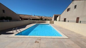 Una piscina rettangolare con bordo piastrellato, circondata da edifici con tetti piani e finestre.