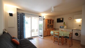 Um espaço de estar compacto com sofá, mesa de jantar com cadeiras, cozinha equipada e televisão.