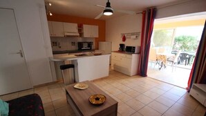 Een ruimtelijk ingerichte leefruimte met kitchenette, eethoek en een schuifpui naar een buitenpatio.