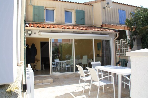 A patio area with a table and chairs, a sliding glass door leading to an indoor space, and a tiled roof.