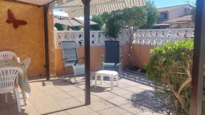 Un patio al aire libre con una mesa y sillas, una valla blanca y un pequeño árbol.