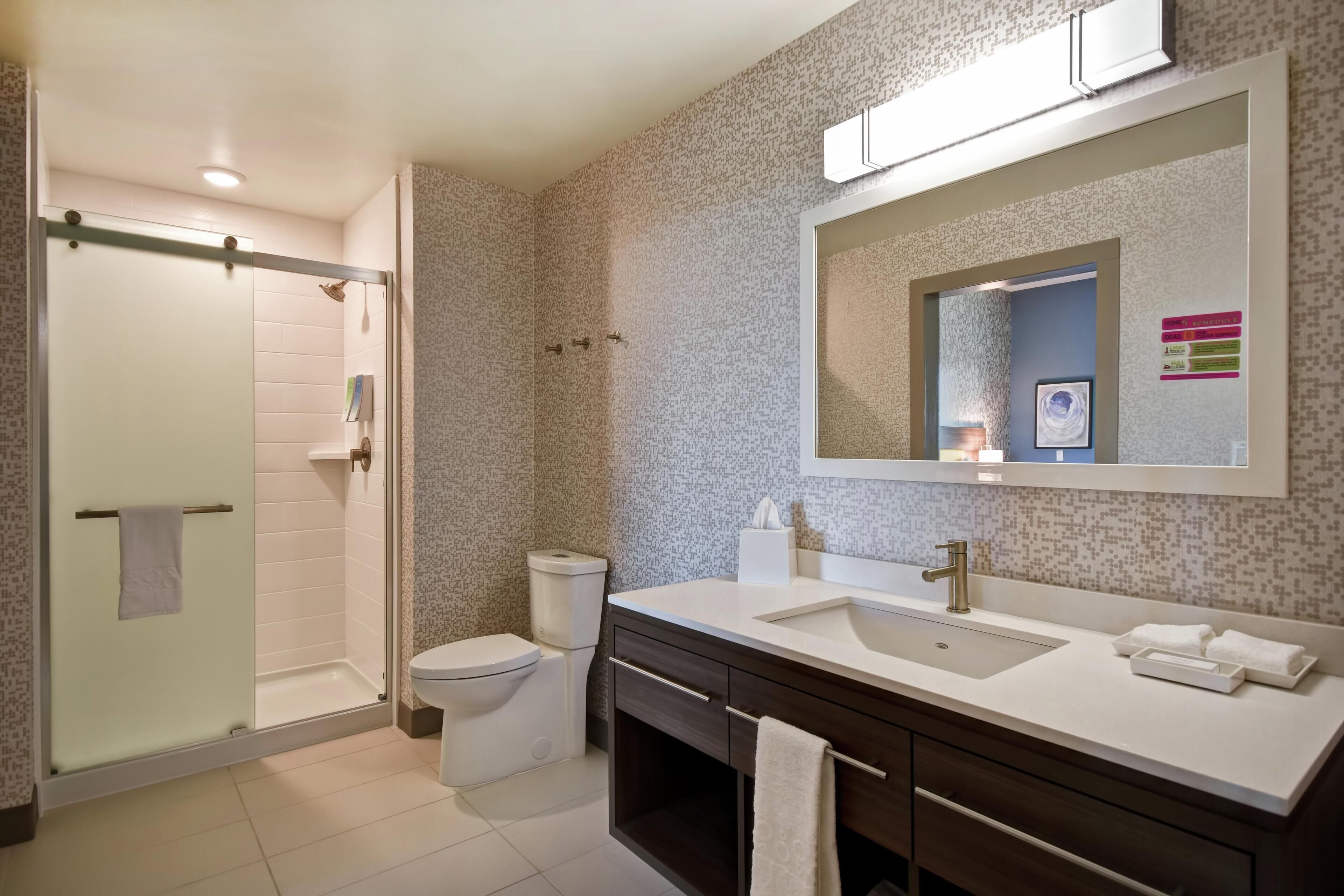 A modern bathroom with a glass shower enclosure, a toilet, a double sink vanity, and a large mirror.