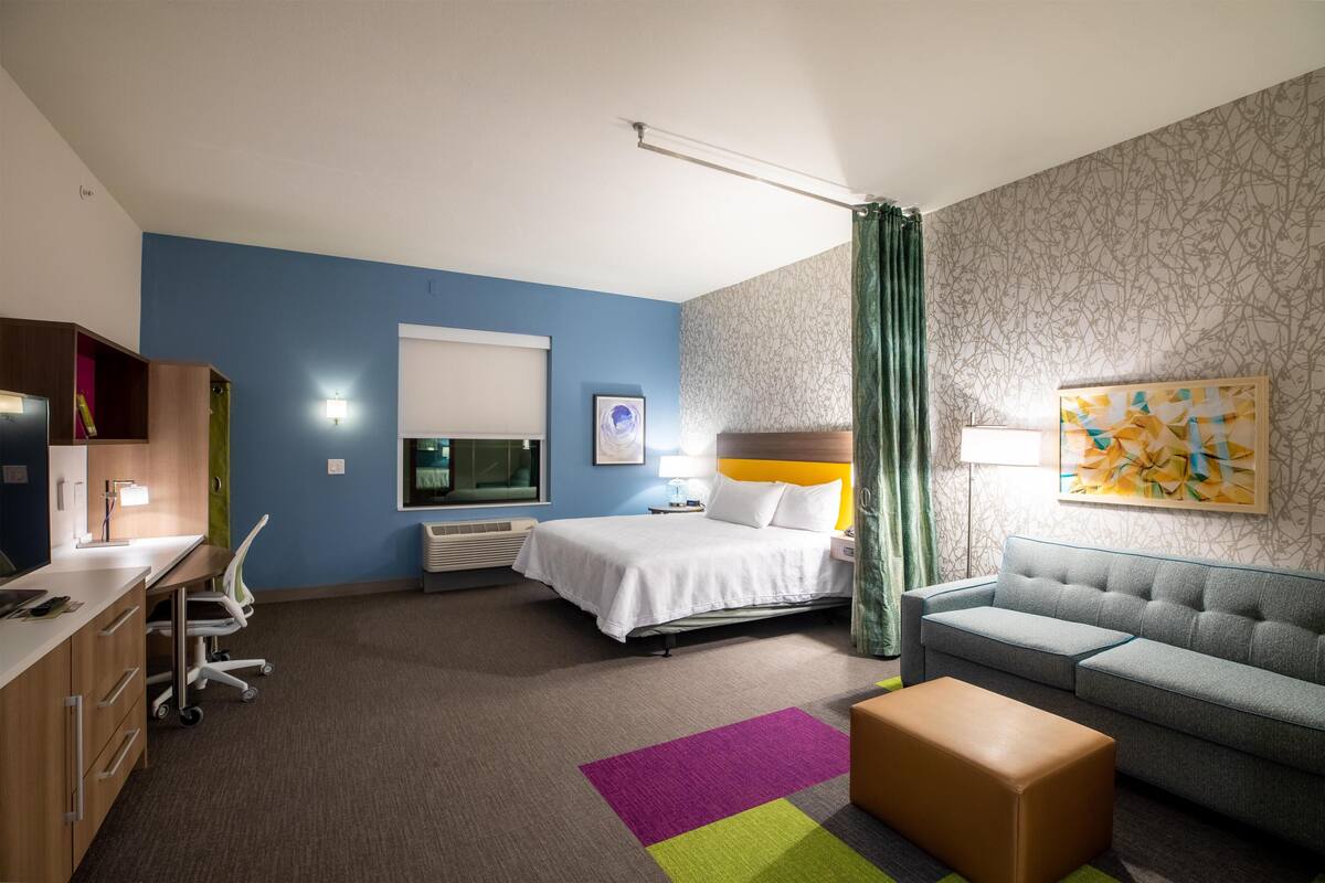 A hotel room with a bed, a desk with a chair, a sofa, and a colorful rug.