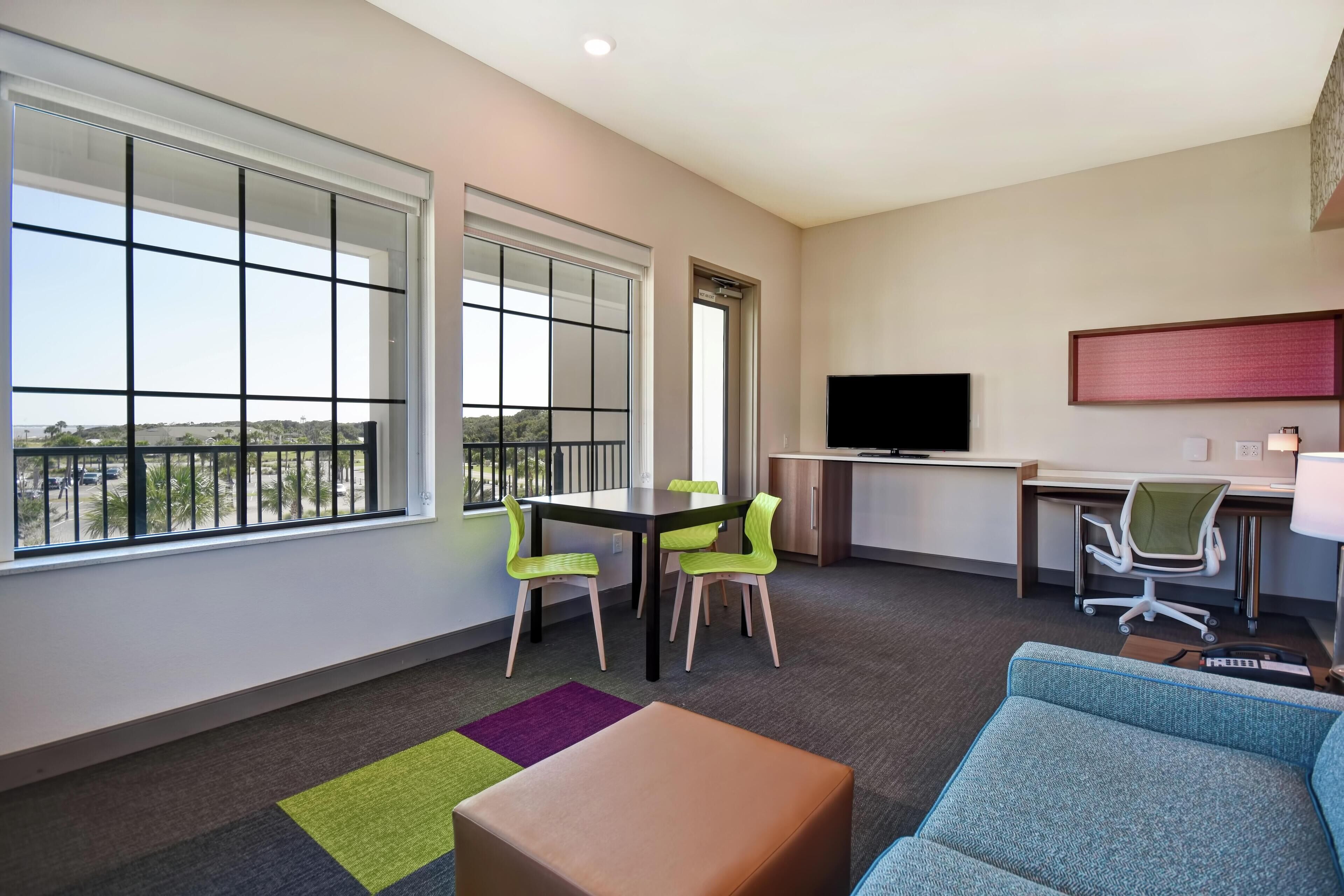A modern hotel room with a balcony, a dining area, a TV, and a sofa.