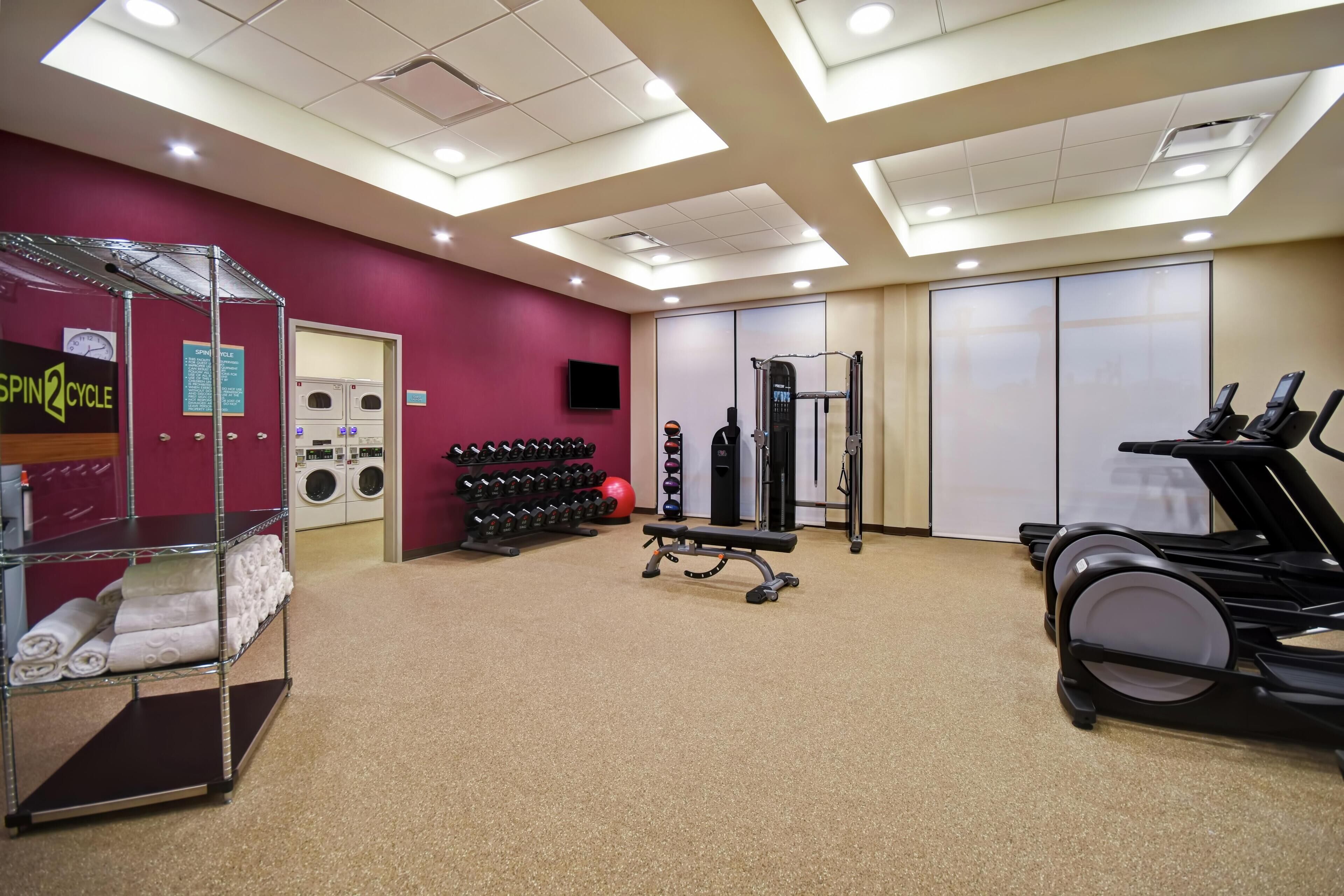 Une salle de sport équipée de matériel d’exercice, d’un tapis de course et d’un téléviseur fixé au mur.