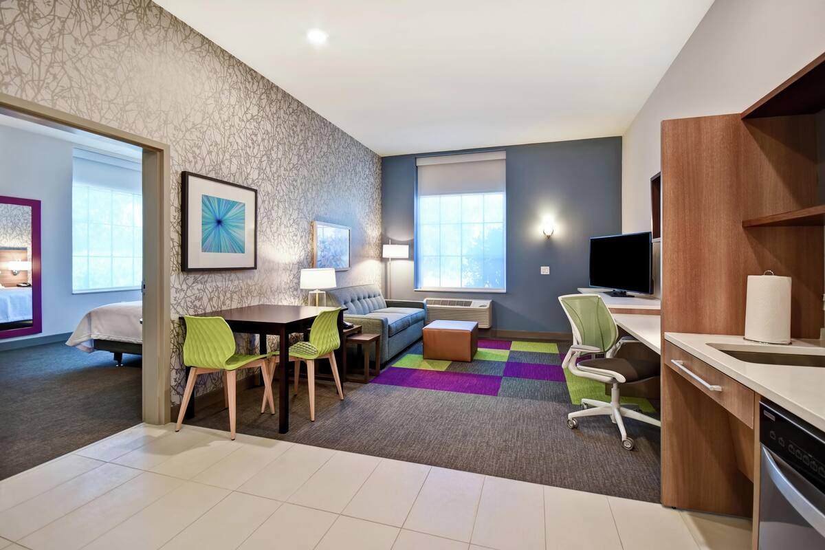 A modern living room with a dining area, a sofa, a TV, and a kitchen area with a dishwasher.