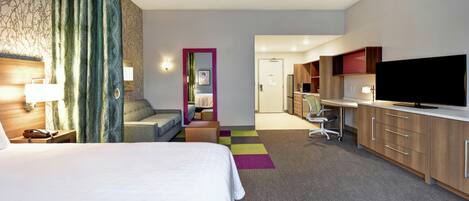 Una habitación de hotel con cama, escritorio, televisor y kitchenette.