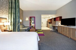 A hotel room with a bed, a desk, a TV, and a kitchenette. - Home2 Suites by Hilton Jekyll Island (Jekyll Island)