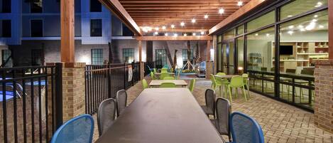 Un espace extérieur aménagé en terrasse, avec une longue table et des chaises, entouré de murs en briques et de grandes fenêtres.