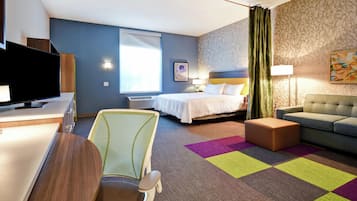 Une chambre d’hôtel avec un lit, un canapé, un bureau avec une télévision, une chaise et une moquette colorée.