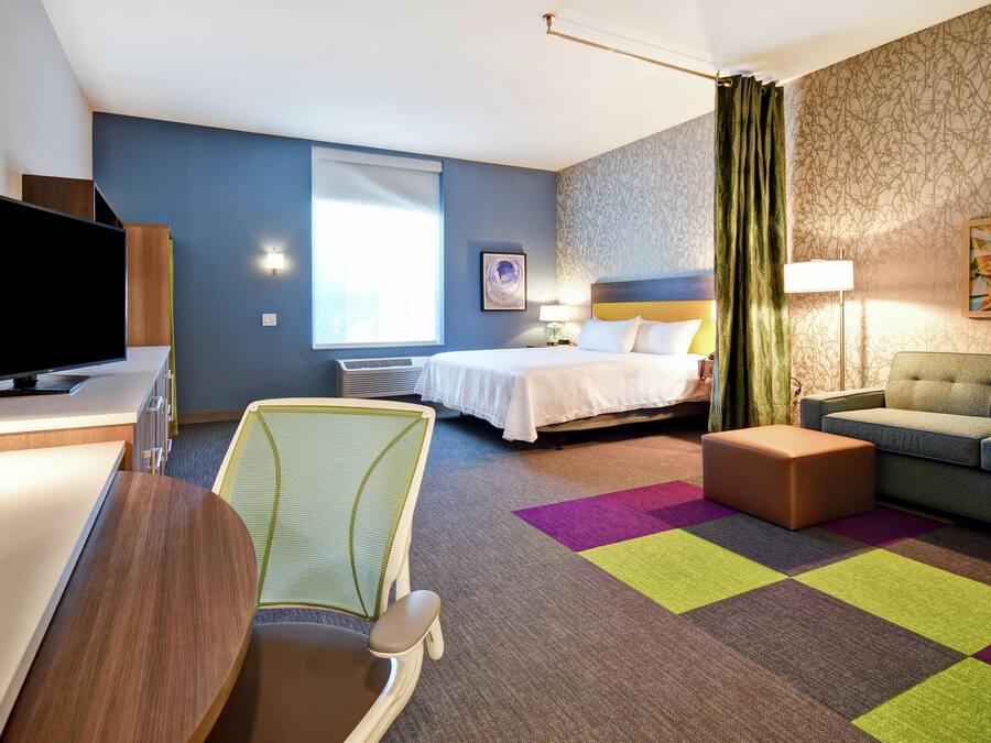 Une chambre d’hôtel avec un lit, un canapé, un bureau avec une télévision, une chaise et une moquette colorée.