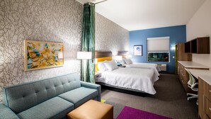 A hotel room with a sofa, two beds, a desk, and a bathroom. - Home2 Suites by Hilton Jekyll Island (Jekyll Island)