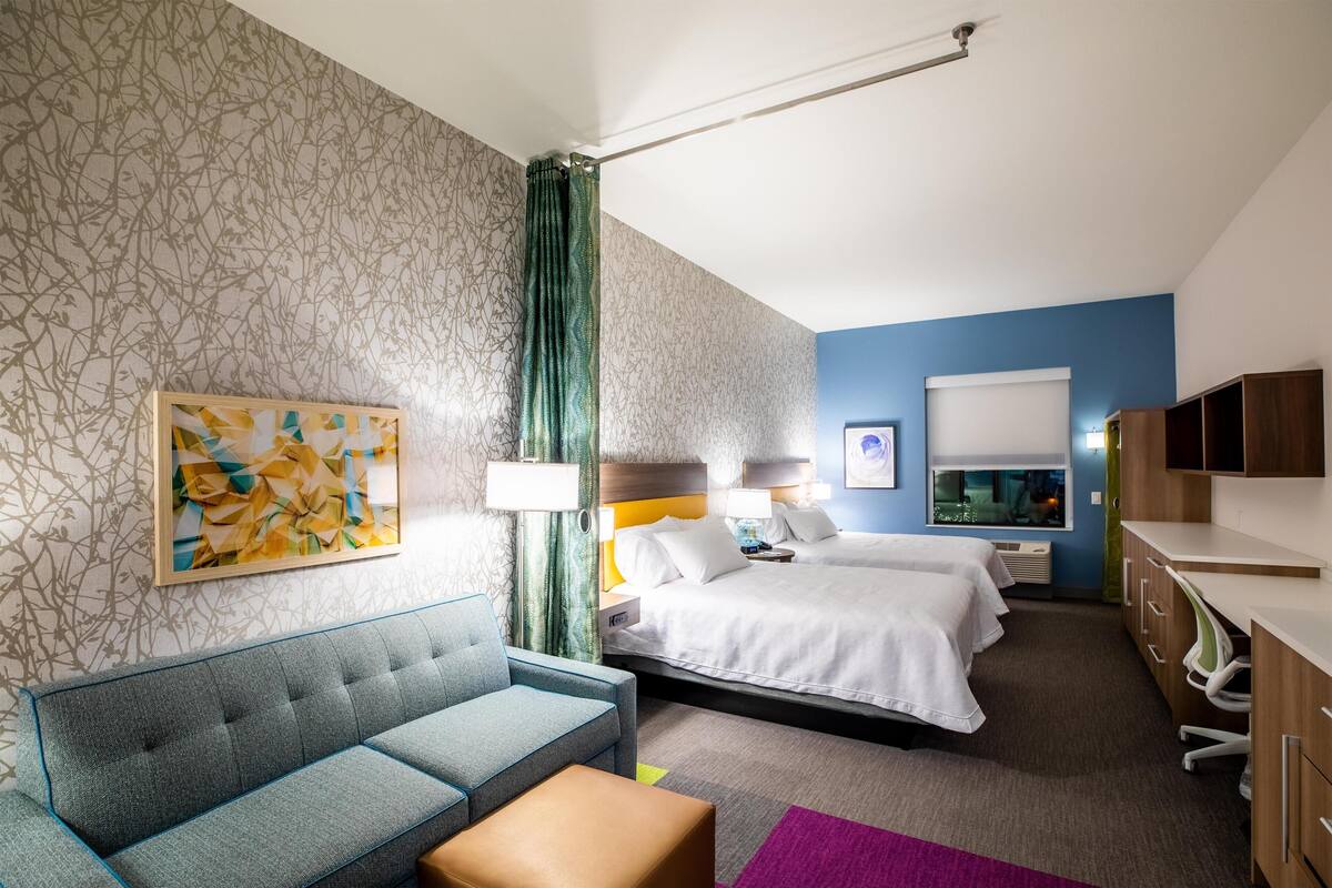 A hotel room with a sofa, two beds, a desk, and a bathroom.