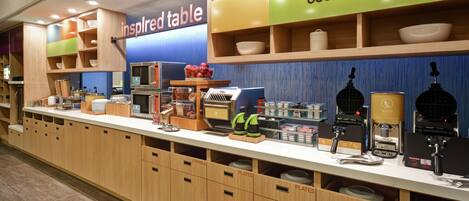 A breakfast bar with a variety of food items and utensils, labeled sections for plates and utensils, and a 'Good Morning' sign.