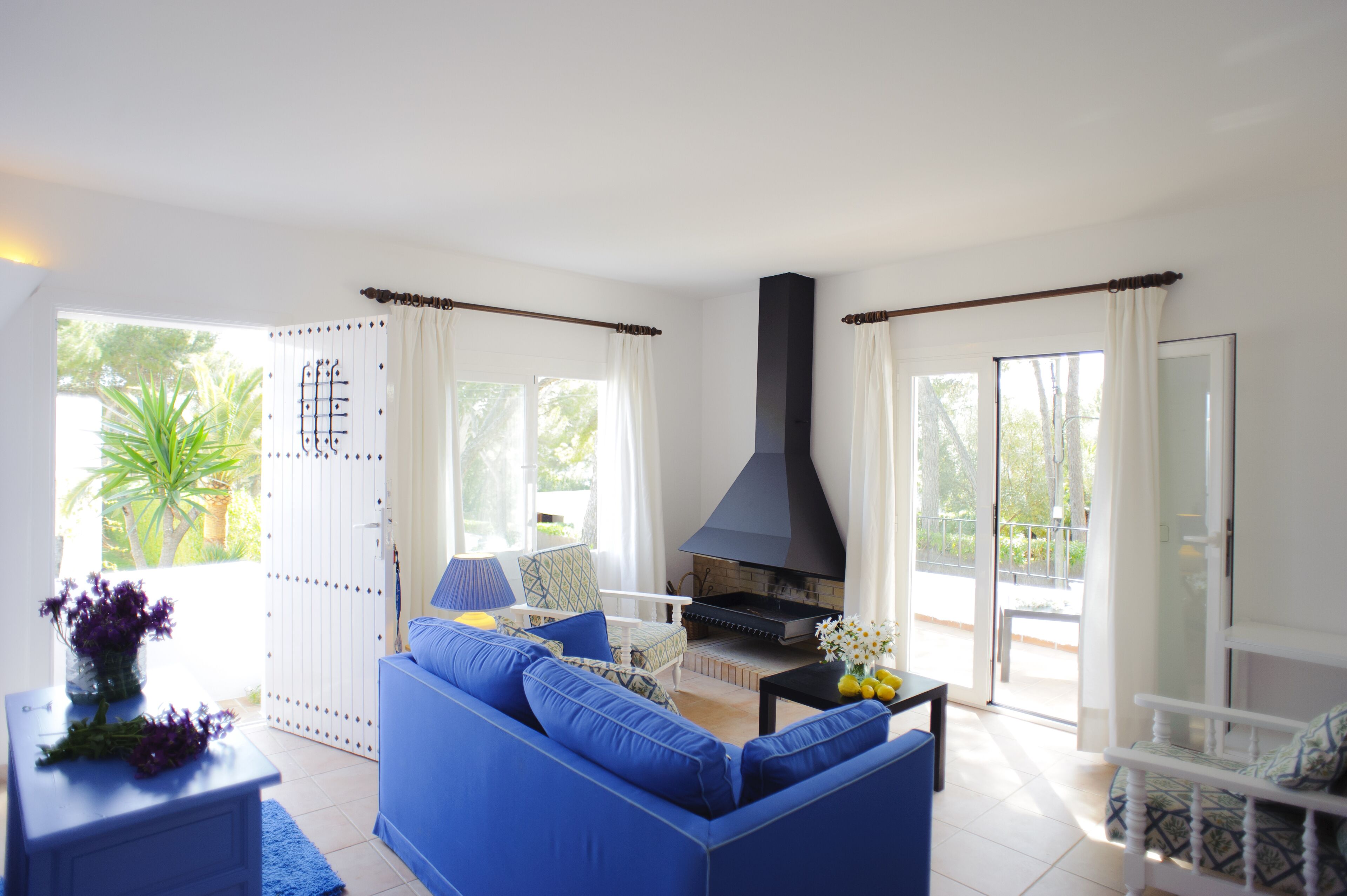 Ein Wohnzimmer mit einem blauen Sofa, einem schwarzen Kamin und Blick ins Freie.