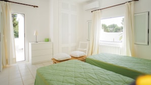 Una camera da letto con due letti, una finestra con tende, un armadio bianco e un tavolino con una lampada.