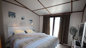 Ein Schlafzimmer mit Bett, Nachttisch, Schreibtisch inklusive Computer und einem Fenster mit Vorhängen.
