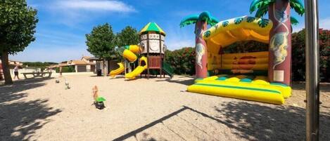 Un patio de recreo al aire libre con toboganes, una estructura para escalar y una zona de juegos con arena.