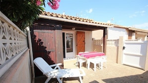 A covered outdoor area with a patio table and chairs, a wooden door, and a white fence.