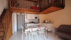 A dining area with a table and chairs, a kitchen with cabinets and appliances, and a staircase leading to an upper level.